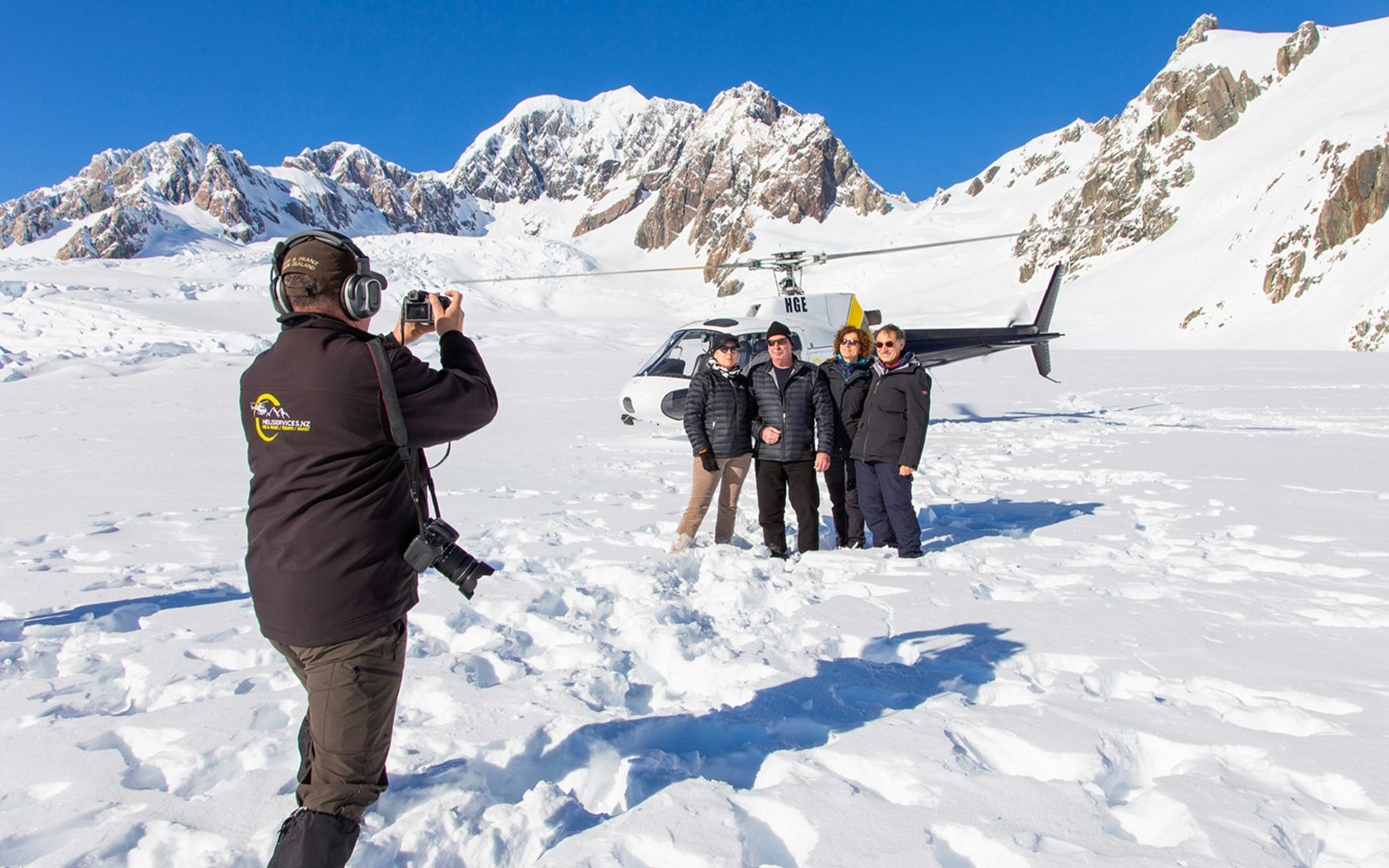 Group posing for a photo on Franz Josef Glacier with a helicopter in the background.