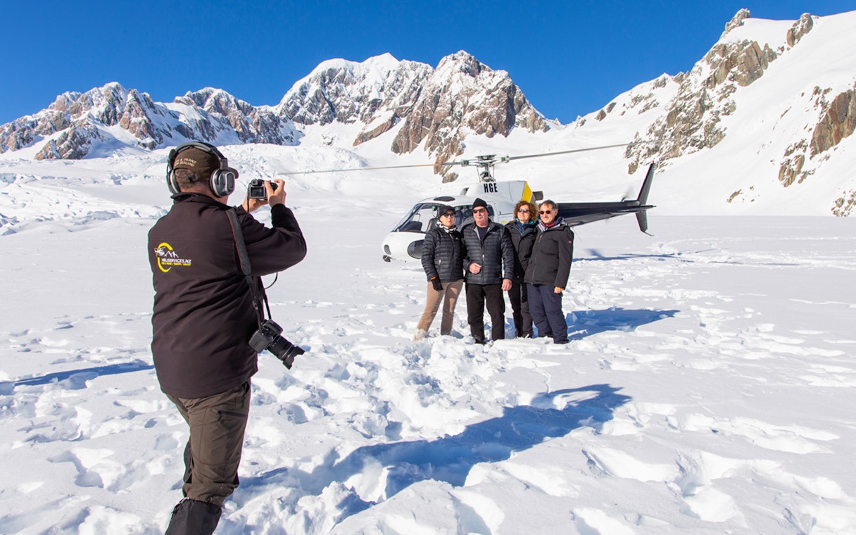 Group posing for a photo on Franz Josef Glacier with a helicopter in the background.