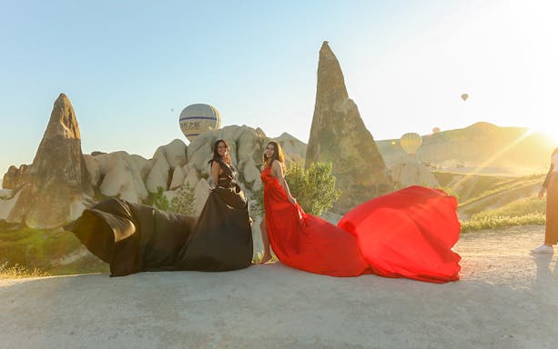 Women in flowing dresses with hot air balloons in Cappadocia during a classic car tour.