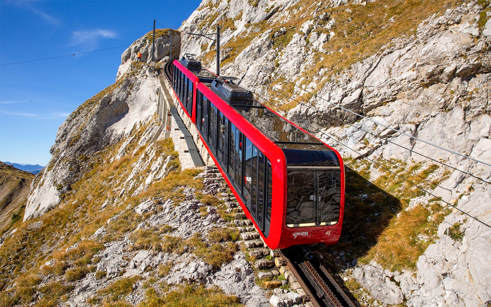 Red cogwheel train ascending Mount Pilatus, Switzerland, with rocky landscape.