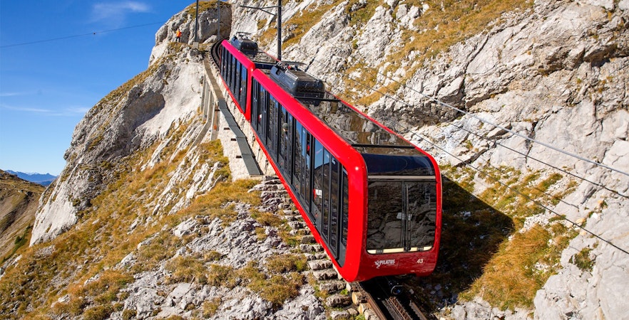 Red cogwheel train ascending Mount Pilatus, Switzerland, with rocky landscape.