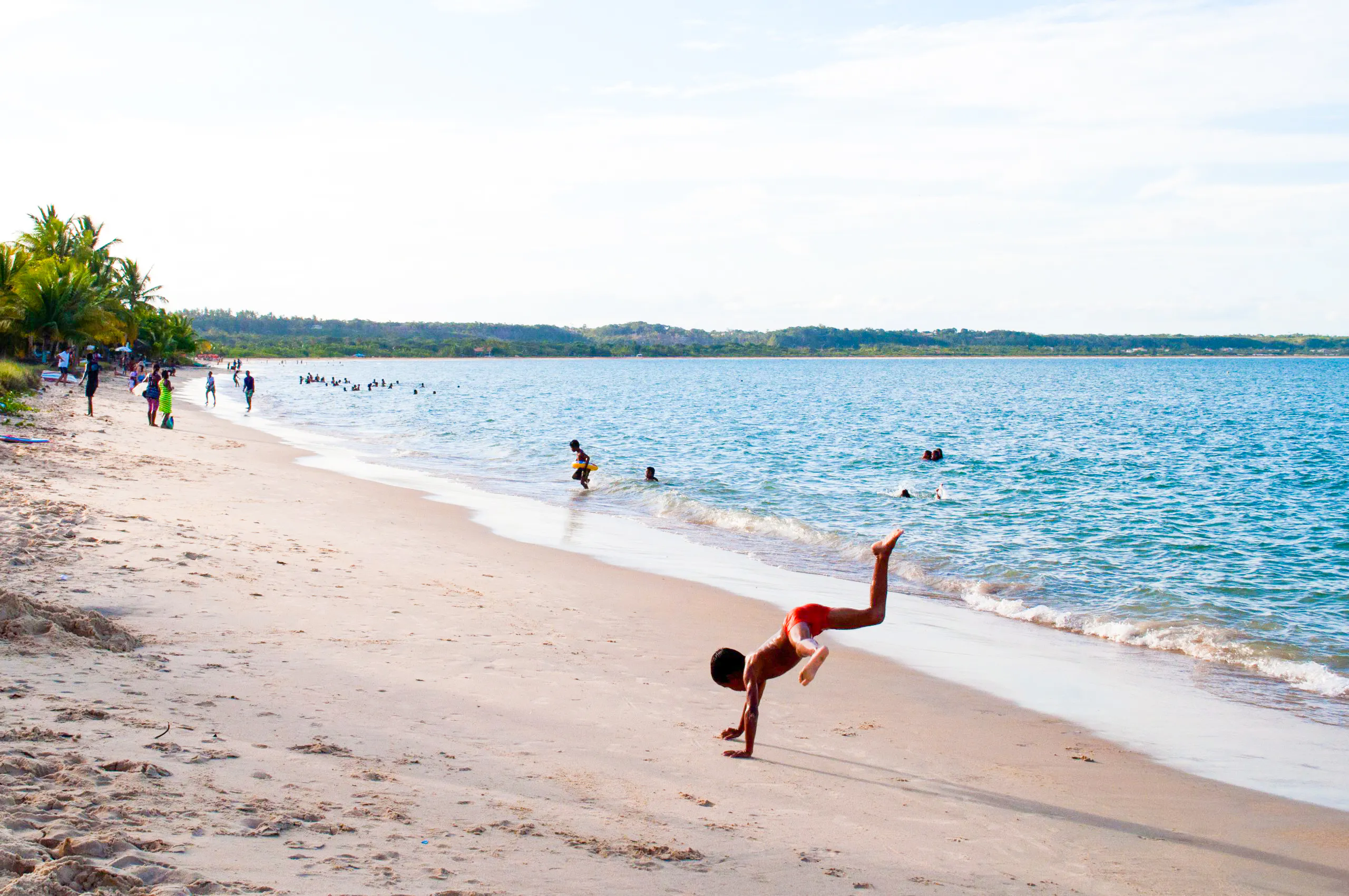 Child playing on Coroa Vermelha beach, Porto Seguro, with people swimming in the ocean.