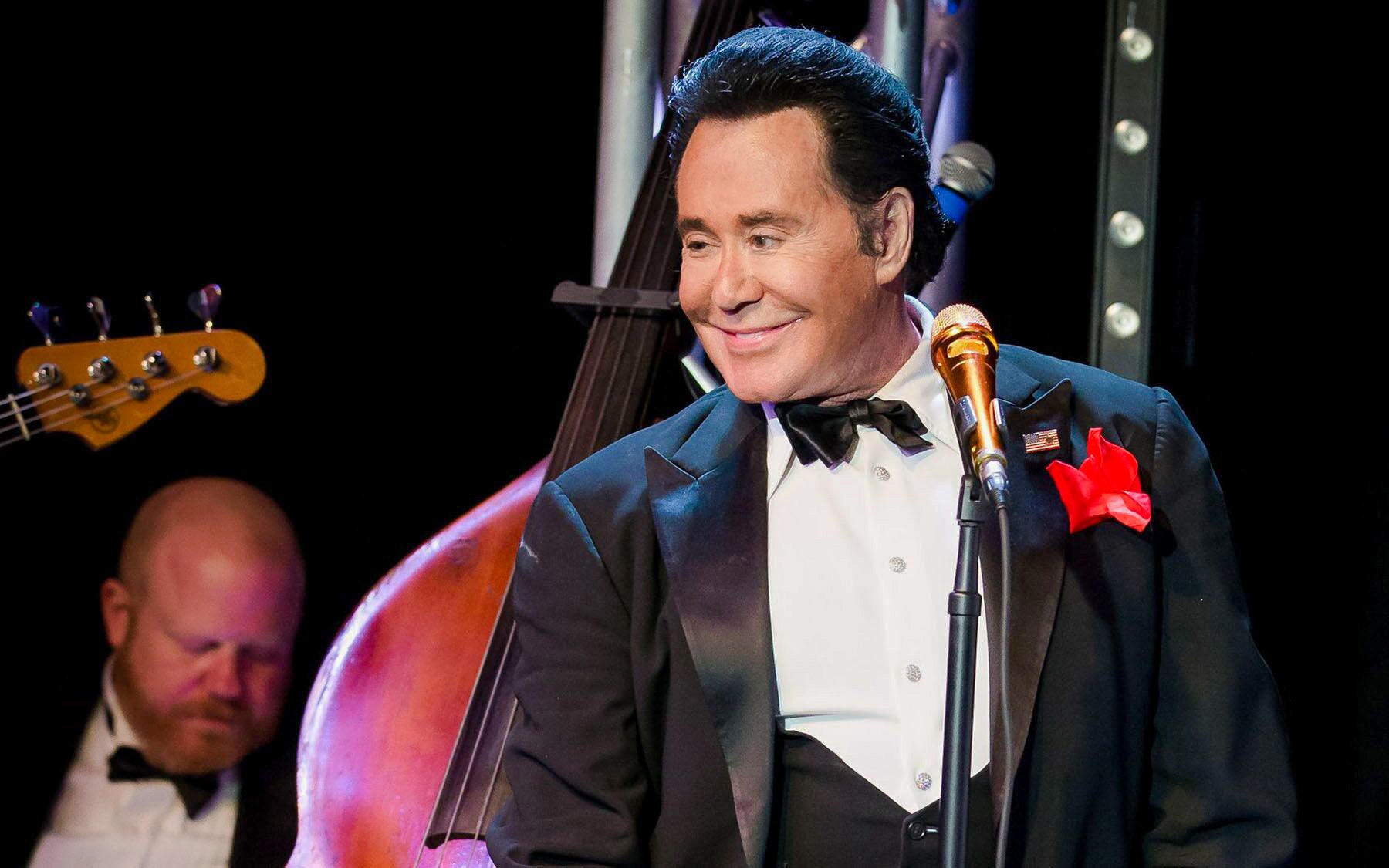 Wayne Newton performing on stage with a double bass in the background.