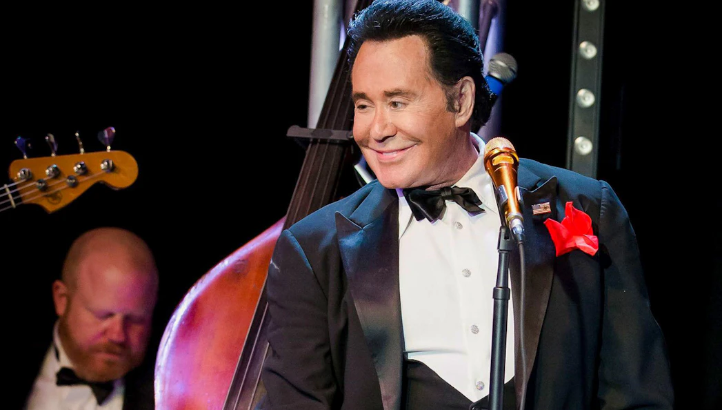 Wayne Newton performing on stage with a double bass in the background.