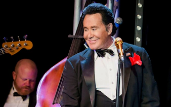 Wayne Newton performing on stage with a double bass in the background.