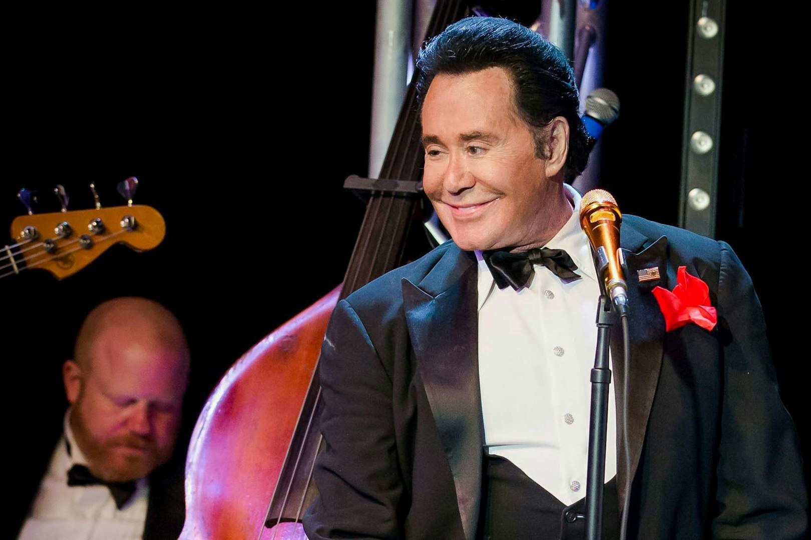 Wayne Newton performing on stage with a double bass in the background.