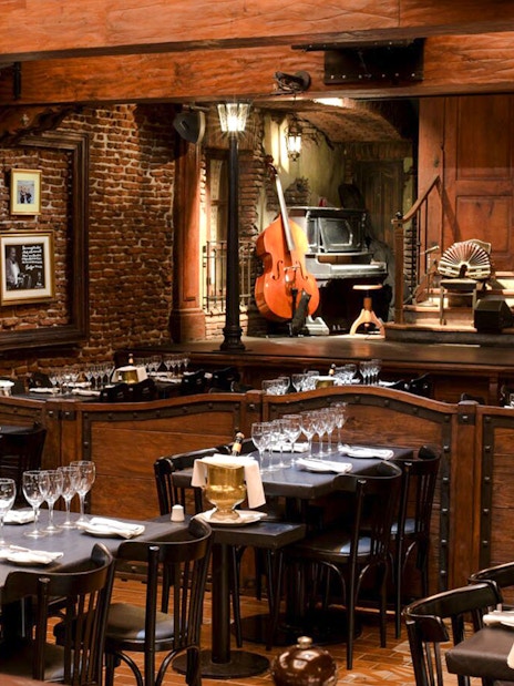 Dining area set for guests at Aljibe Tango Show with stage and musical instruments.