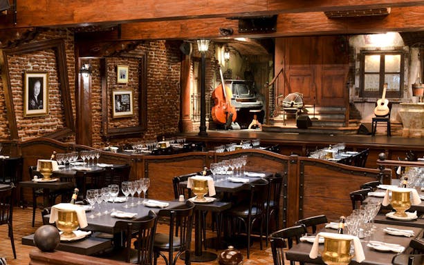 Dining area set for guests at Aljibe Tango Show with stage and musical instruments.