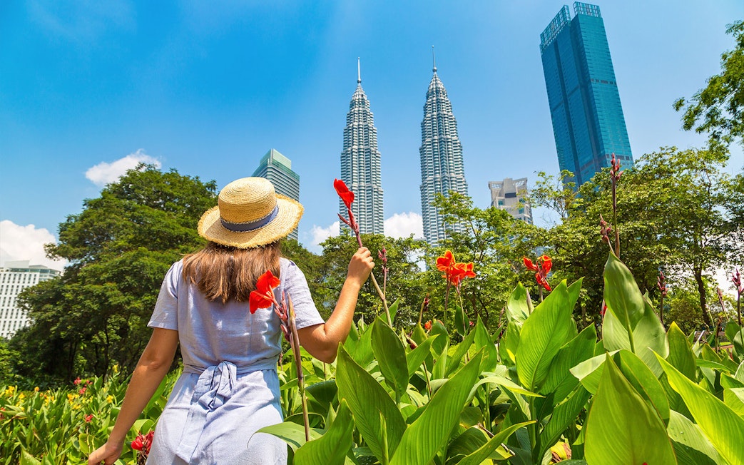 Person in a hat holding flowers near Petronas Towers, Kuala Lumpur.