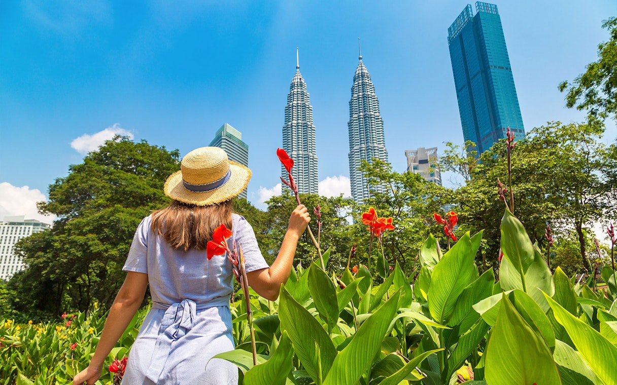 Person in a hat holding flowers near Petronas Towers, Kuala Lumpur.