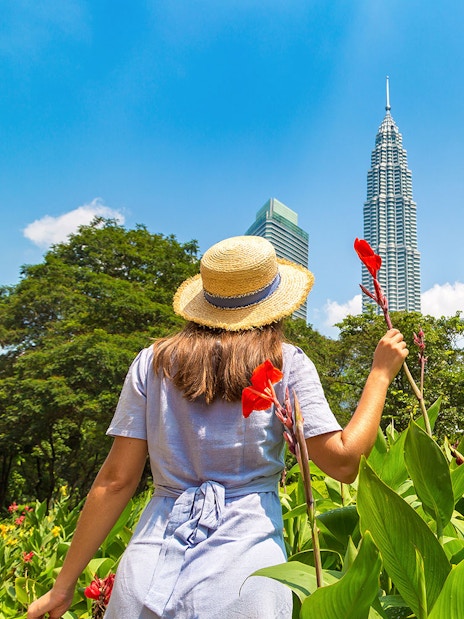 Person in a hat holding flowers near Petronas Towers, Kuala Lumpur.