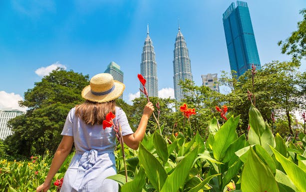 Person in a hat holding flowers near Petronas Towers, Kuala Lumpur.