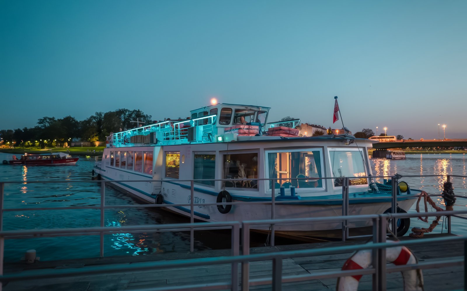 Cruise boat docked on Vistula River at dusk with city lights in the background.