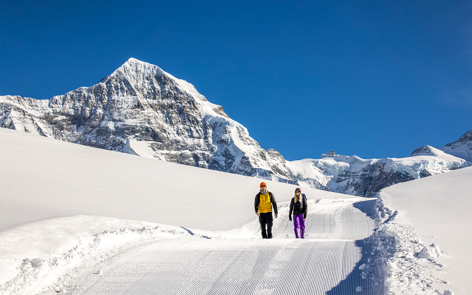 Hikers trekking snowy trails with views of Grindelwald's alpine landscape.