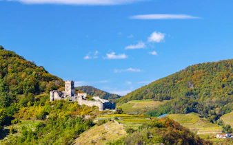 Hinterhaus castle ruins on a hill surrounded by lush greenery and vineyards.