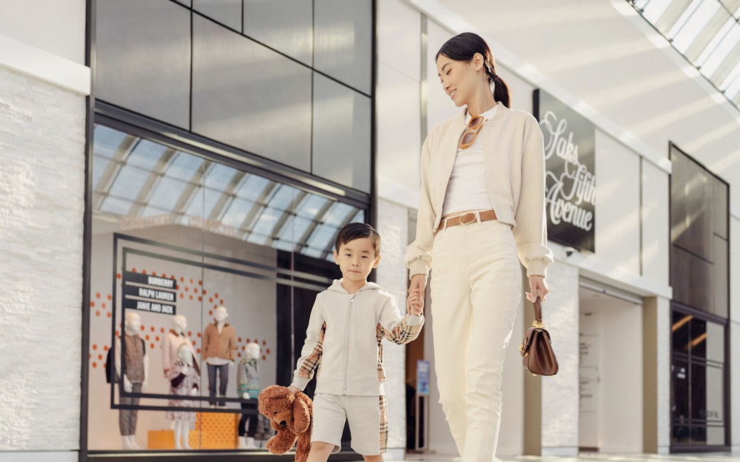 Parent and child holding hands while shopping at a mall.