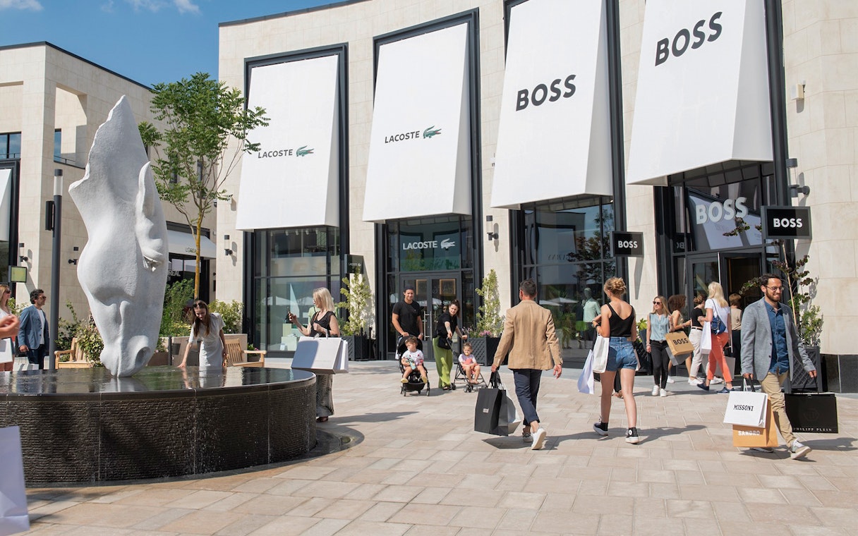 Shoppers walking near a fountain at an outdoor shopping center.