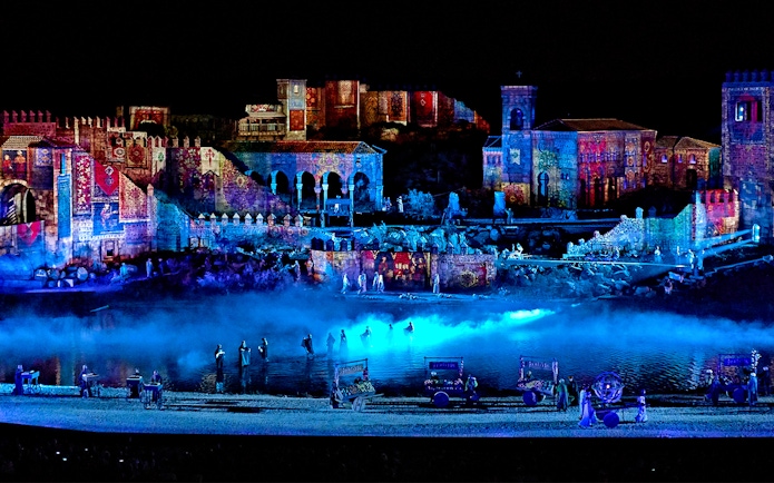 The Dream of Toledo Night Show with illuminated historic buildings and performers by a river.