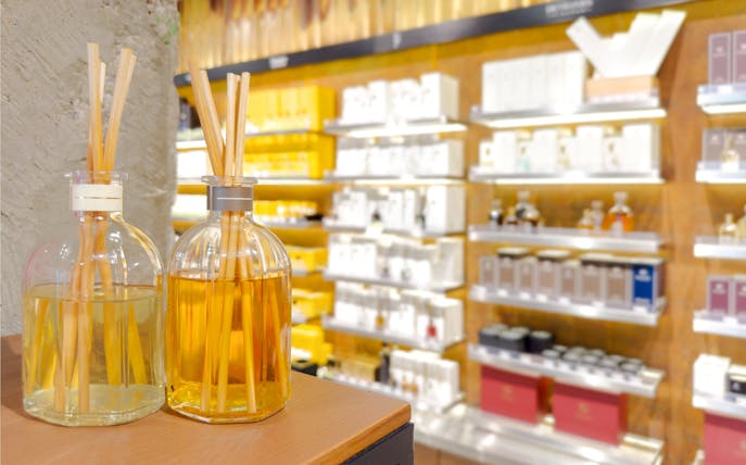 Reed diffusers on display in a perfume shop with shelves of fragrances in the background.