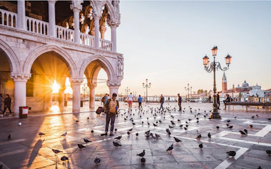 Venice sunrise at St. Mark's Square with people and pigeons, near Doge's Palace.