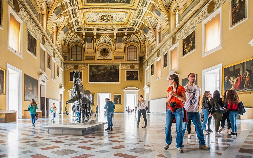 Visitors exploring the grand hall of the Archaeological Museum of Naples with statues and paintings.