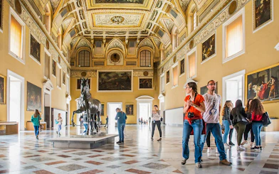 Visitors exploring the grand hall of the Archaeological Museum of Naples with statues and paintings.