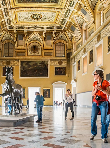 Visitors exploring the grand hall of the Archaeological Museum of Naples with statues and paintings.
