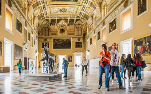Visitors exploring the grand hall of the Archaeological Museum of Naples with statues and paintings.