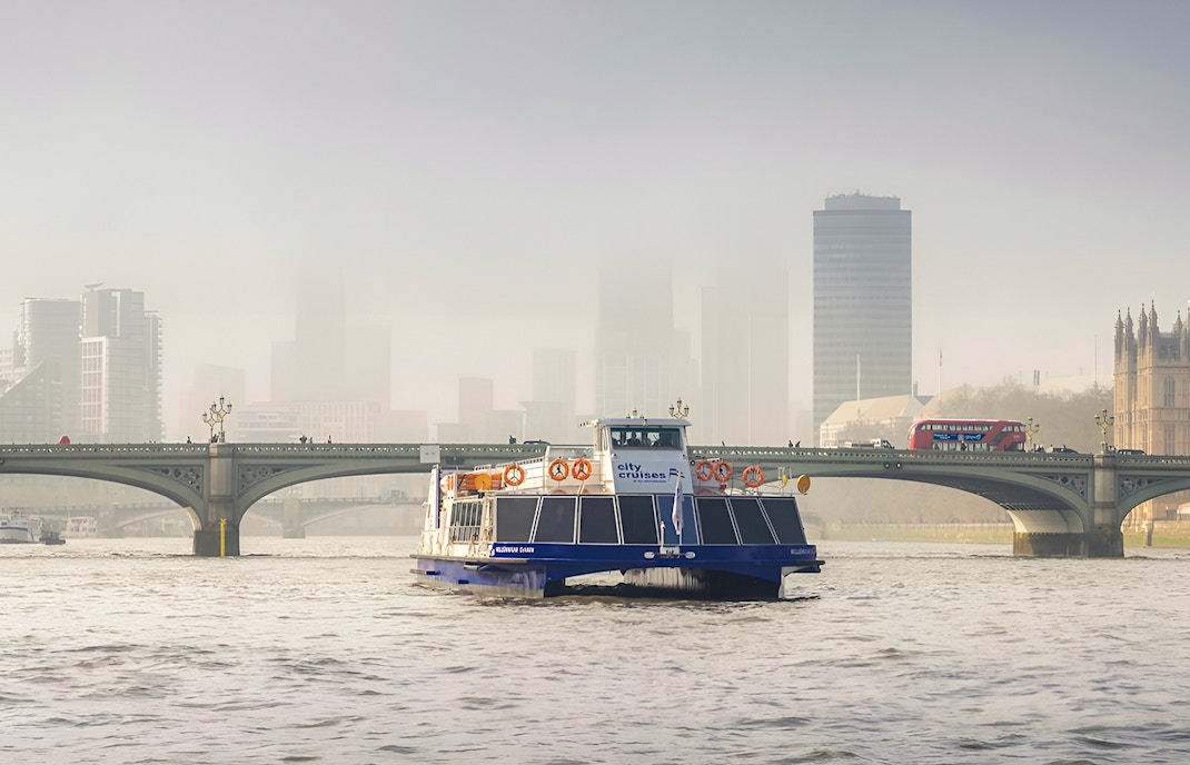 Cruise boat on the Thames River with Westminster Bridge and London skyline in the background.