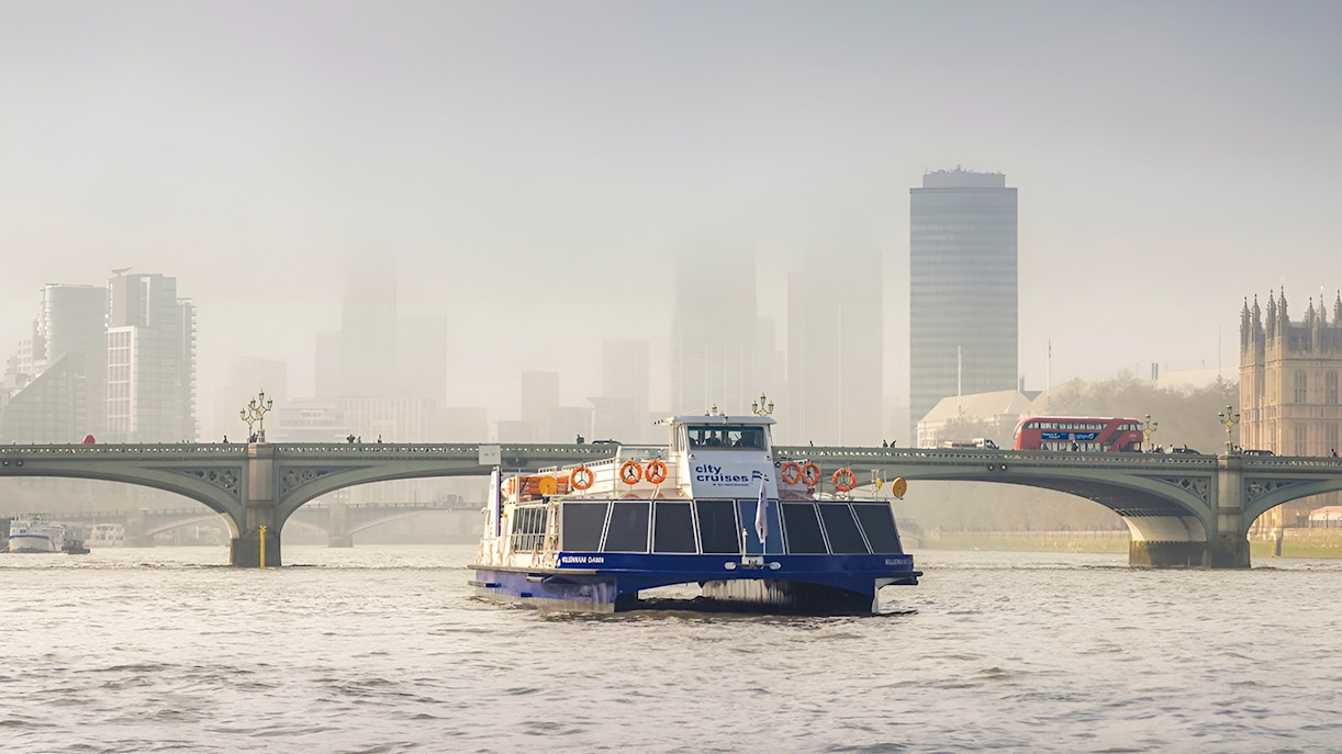 Cruise boat on the Thames River with Westminster Bridge and London skyline in the background.