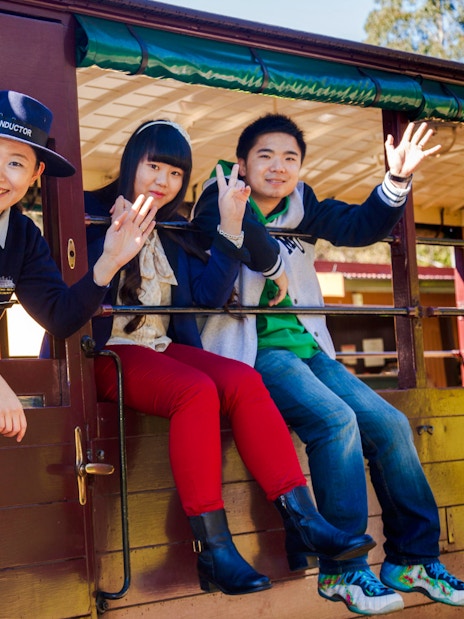 Conductor and passengers wave from a Puffing Billy carriage on a Melbourne tour.