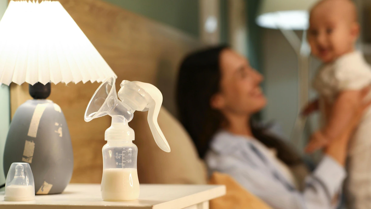 Breast pump on nightstand with mother holding baby in bedroom.
