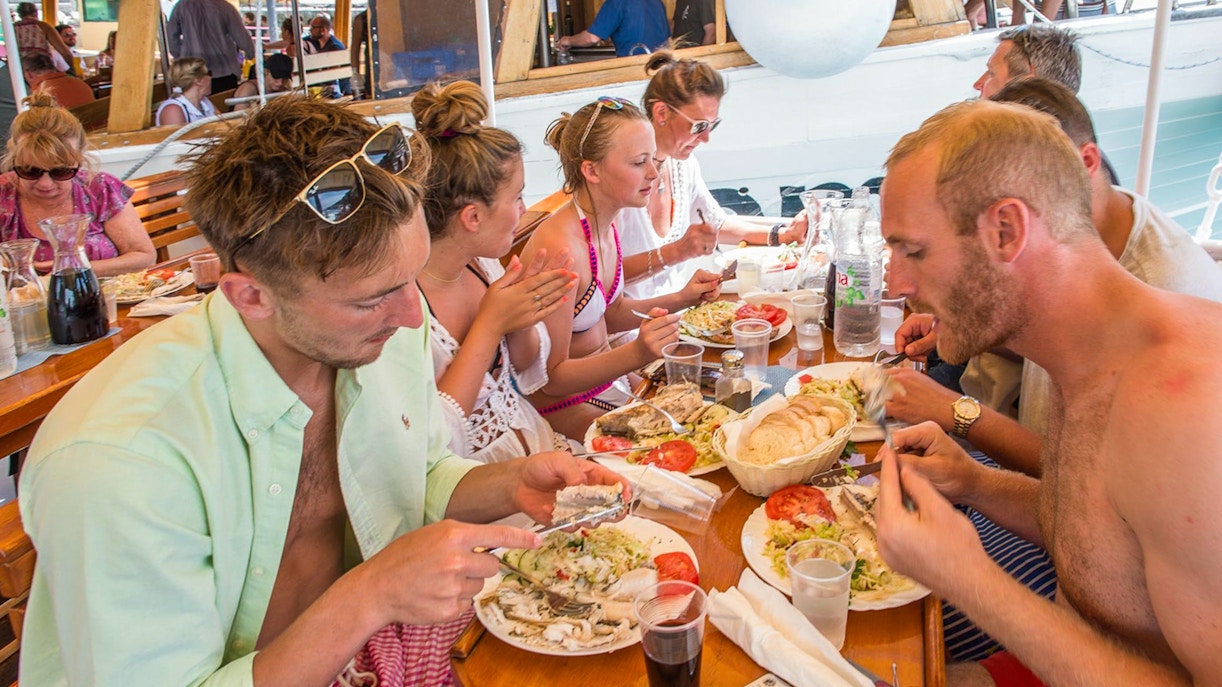 Passengers dining on a boat with plates of fish, salad, and bread.