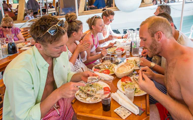 Passengers dining on a boat with plates of fish, salad, and bread.