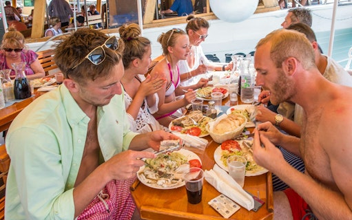 Passengers dining on a boat with plates of fish, salad, and bread.