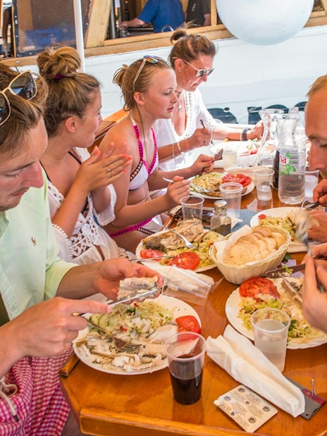 Passengers dining on a boat with plates of fish, salad, and bread.