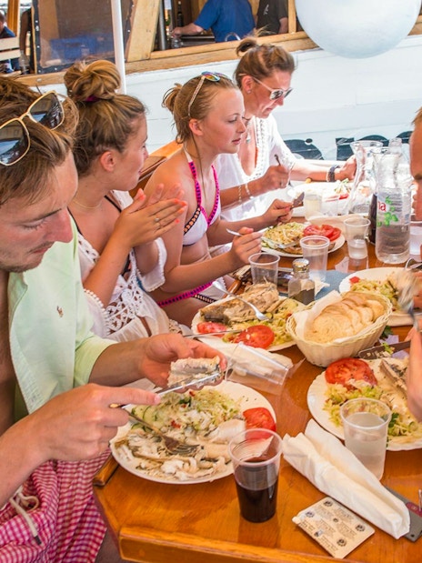 Passengers dining on a boat with plates of fish, salad, and bread.
