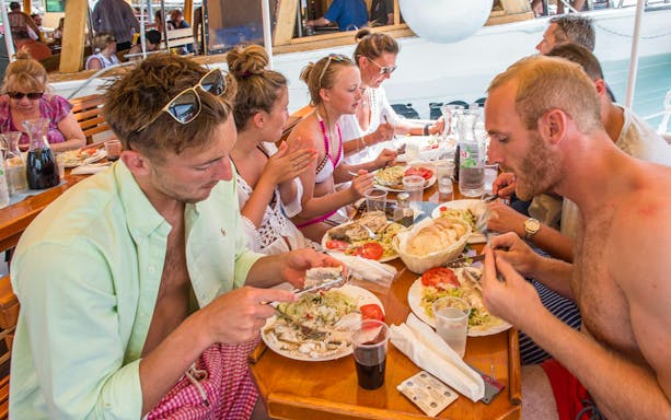 Passengers dining on a boat with plates of fish, salad, and bread.