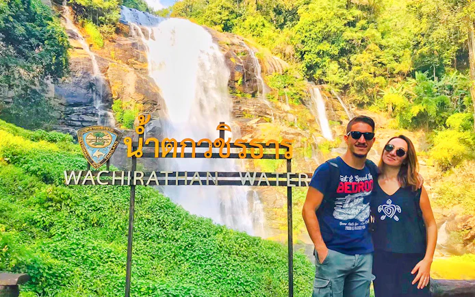 Couple in front of Wachirathan Waterfall sign on Doi Inthanon tour, Thailand.