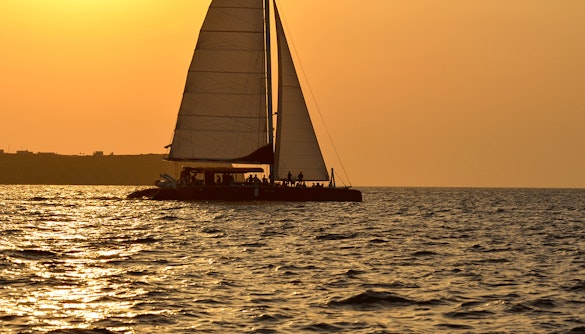 Catamaran sailing at sunset during Santorini cruise with BBQ and open bar.