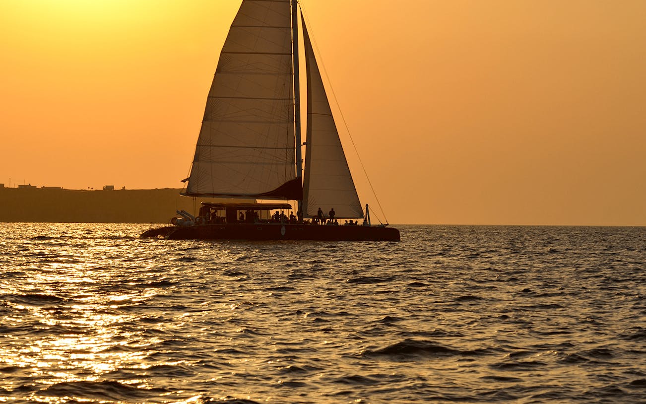 Catamaran sailing at sunset during Santorini cruise with BBQ and open bar.