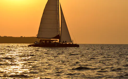 Catamaran sailing at sunset during Santorini cruise with BBQ and open bar.