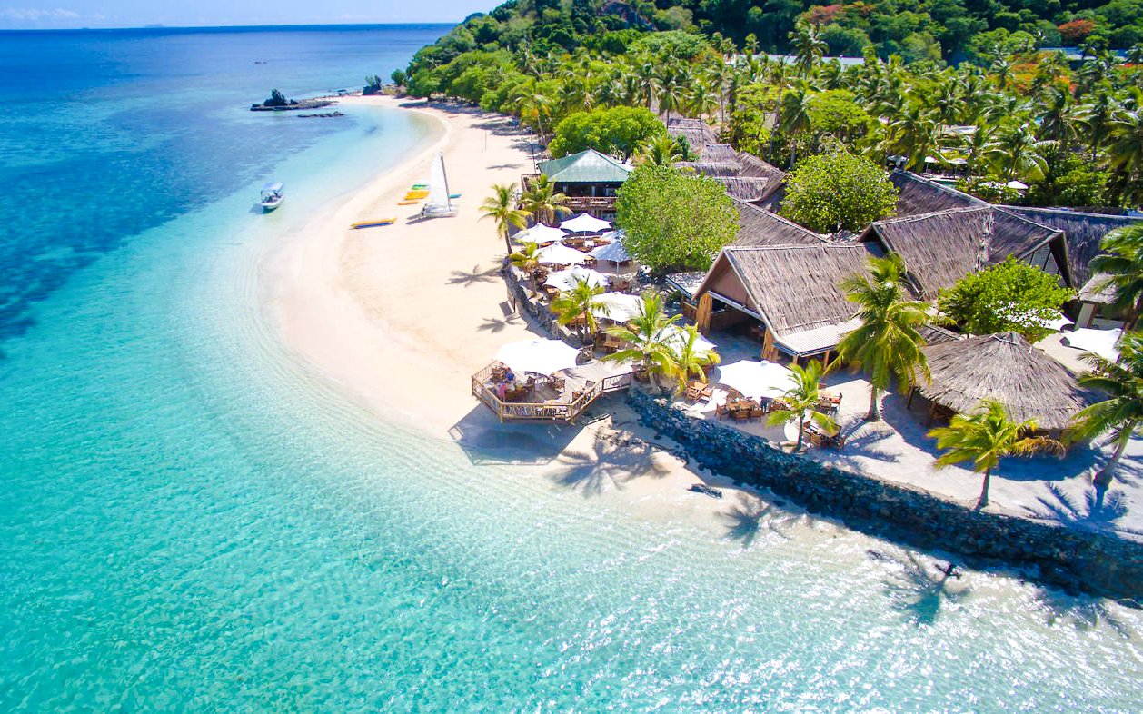 Aerial view of Castaway Island, Fiji with beachfront huts and turquoise waters.