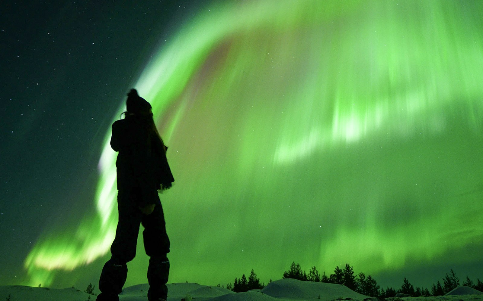 Person photographing Northern Lights on snowy landscape during Premium Small Group Northern Lights Tour.