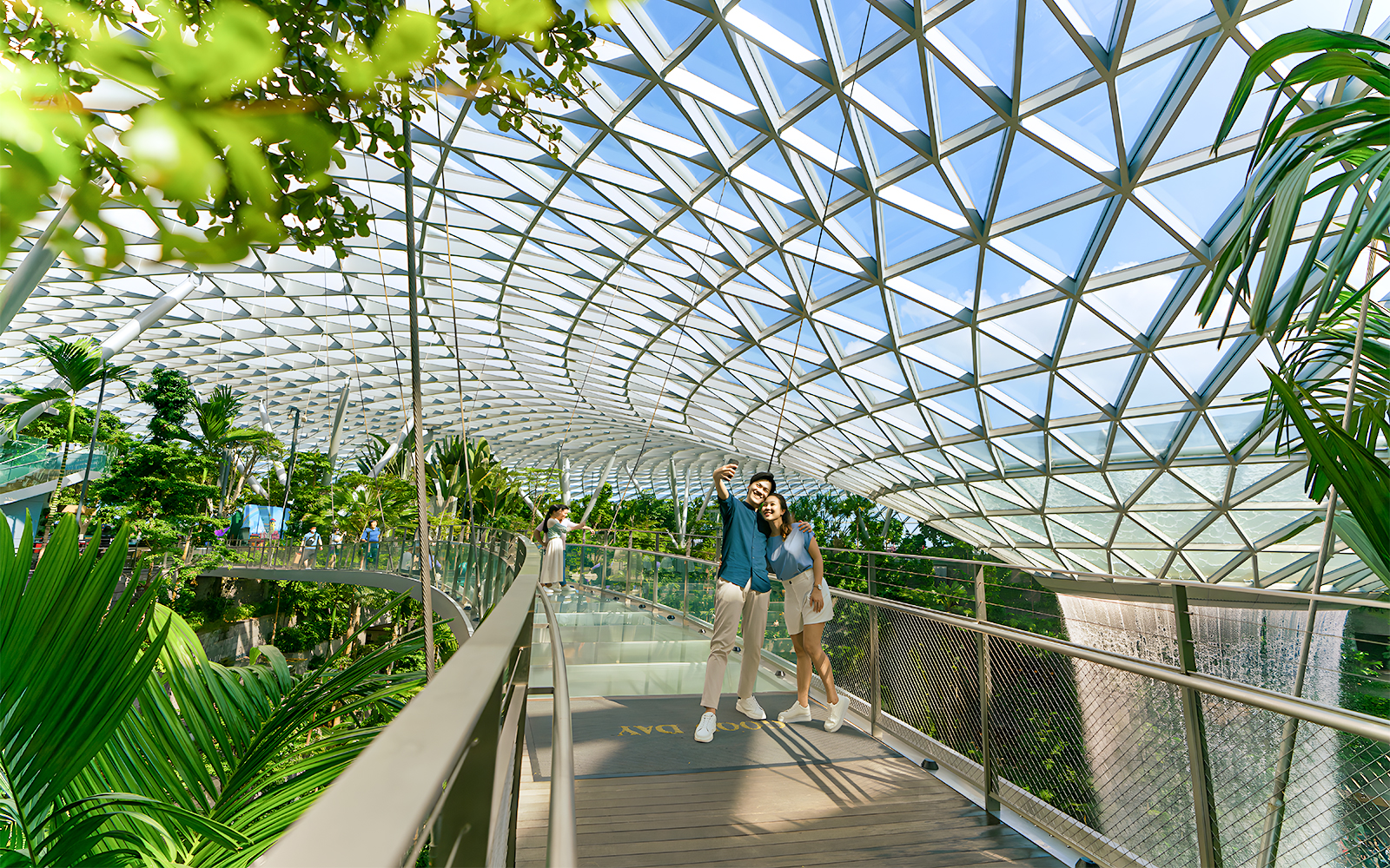 Couple taking selfie on walkway at Jewel Changi Airport, Singapore, under glass dome.