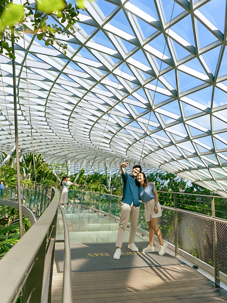 Couple taking selfie on walkway at Jewel Changi Airport, Singapore, under glass dome.