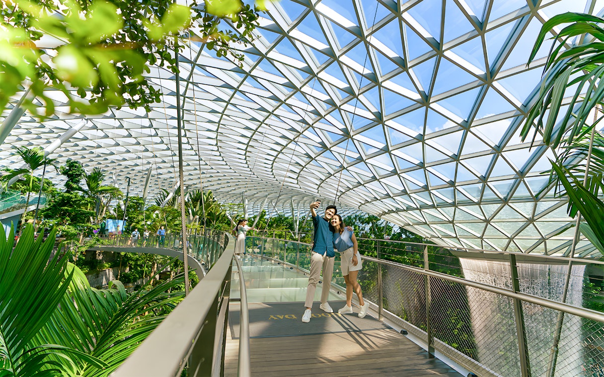 Couple taking selfie on walkway at Jewel Changi Airport, Singapore, under glass dome.