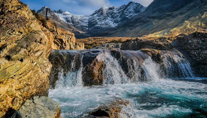 Fairy Pools waterfall with rocky landscape and snow-capped mountains, Isle of Skye, Scotland.