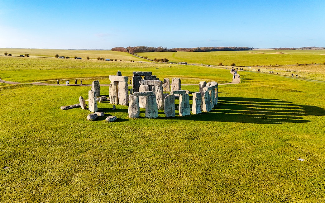 Stonehenge stone circle on a sunny day with green fields, viewed from above.