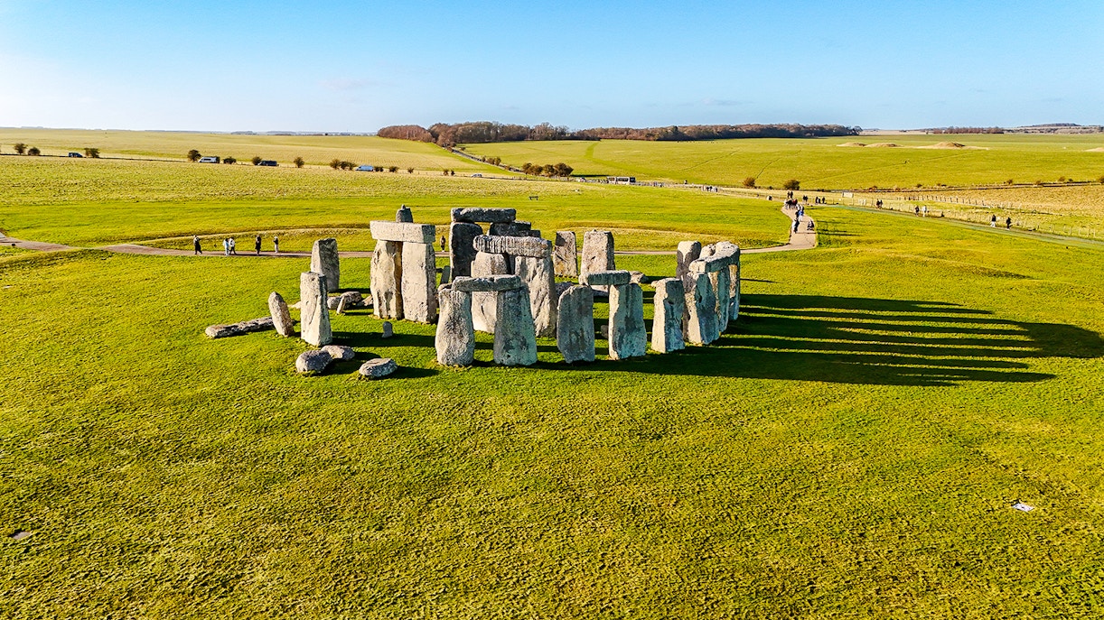 Stonehenge stone circle on a sunny day with green fields, viewed from above.